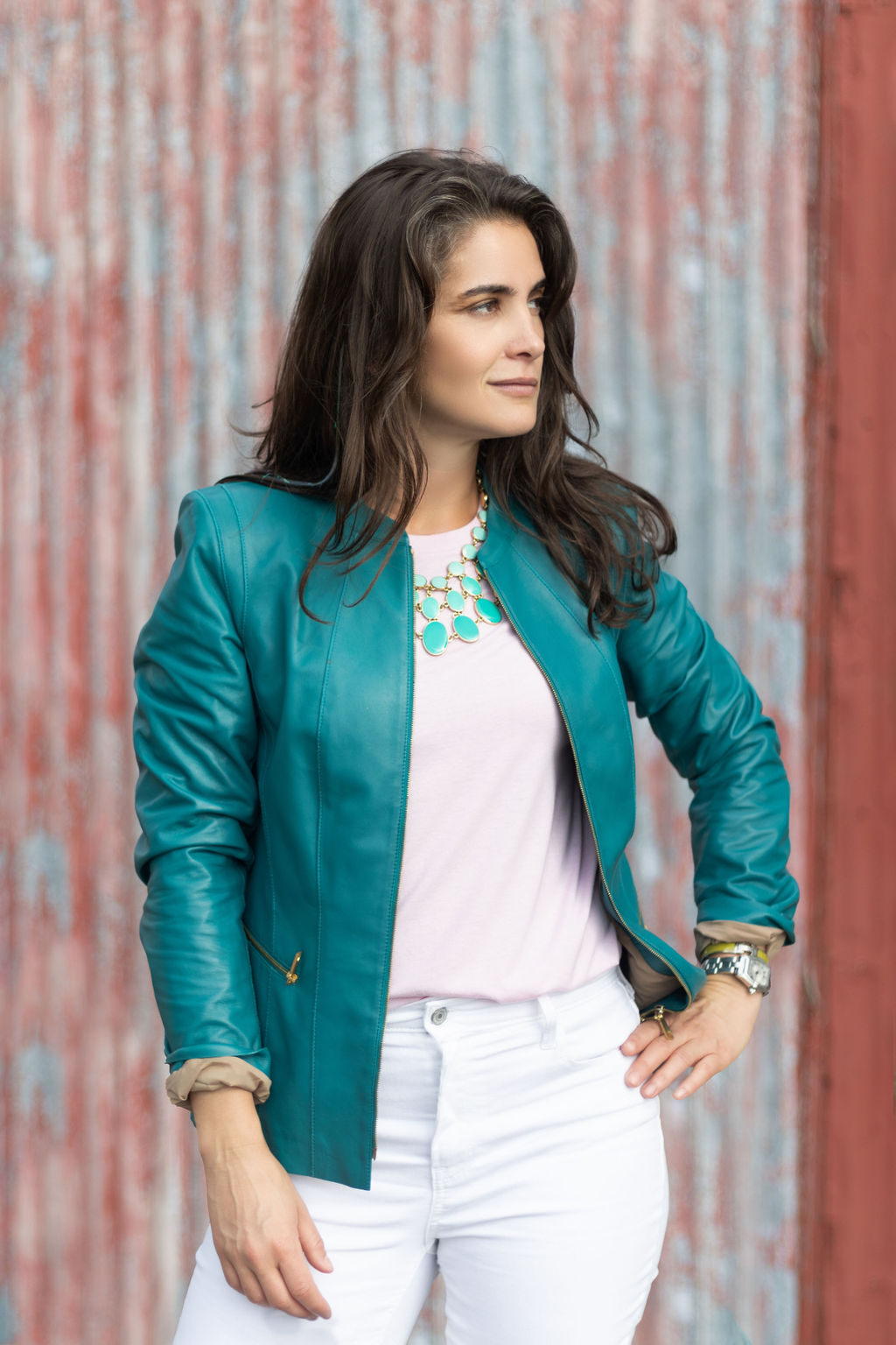 Woman in turquoise leather jacket and pink shirt in front of a red and blue wall.