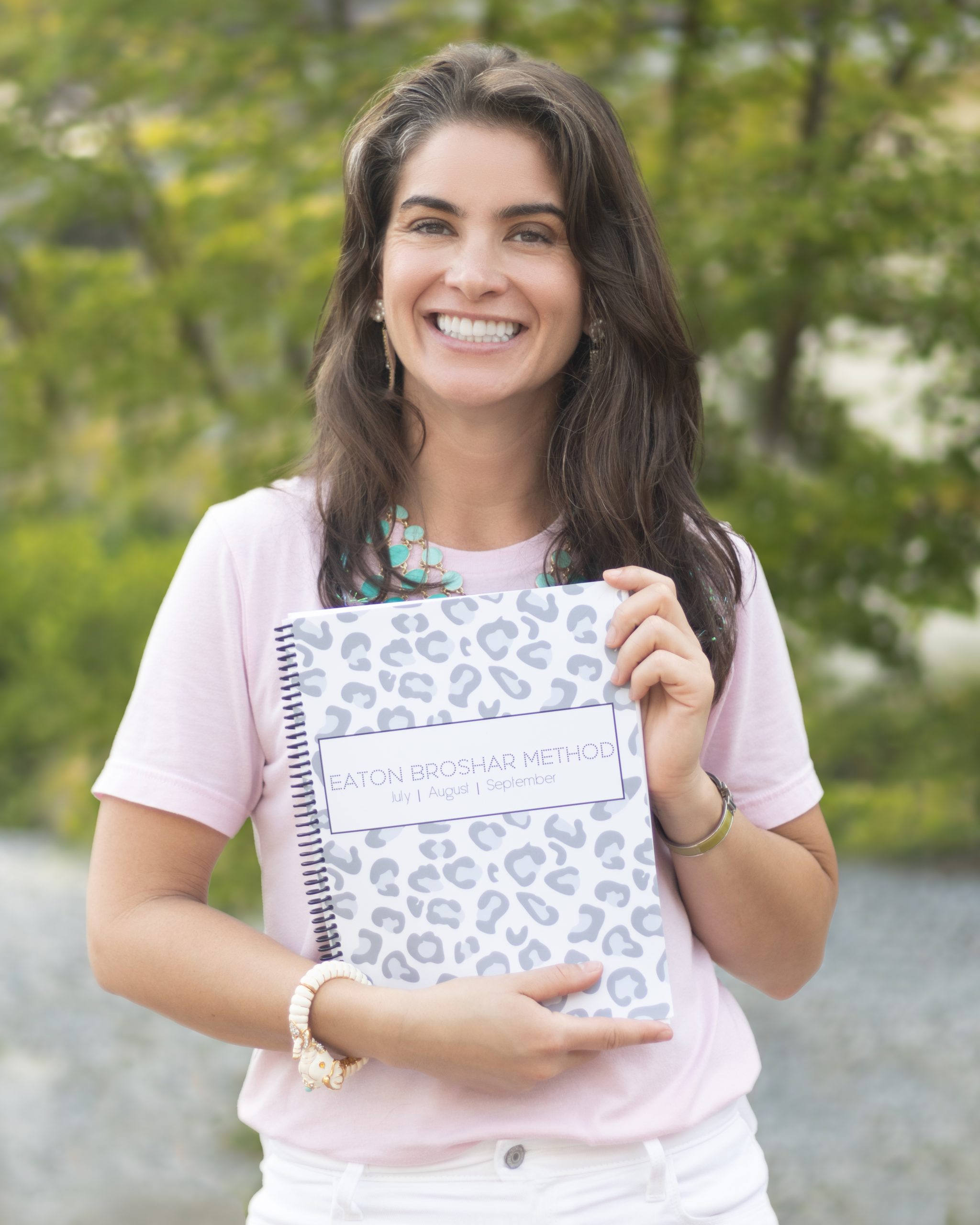 Woman in pink shirt holding a leopard print Eaton Broshar Method Workbook.